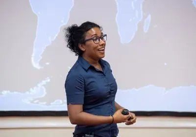 Izzy Jayasinghe stands in front of a projection of a map, looking as though she is speaking